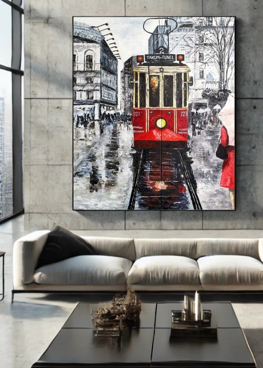 A monochrome artwork capturing a rainy night scene at Taksim Square with a red tram and a woman wearing a red coat holding an umbrella hanging on a stone wall over a modern sofa in a modern living room. The image has a textured surface and uses a palette knife technique.