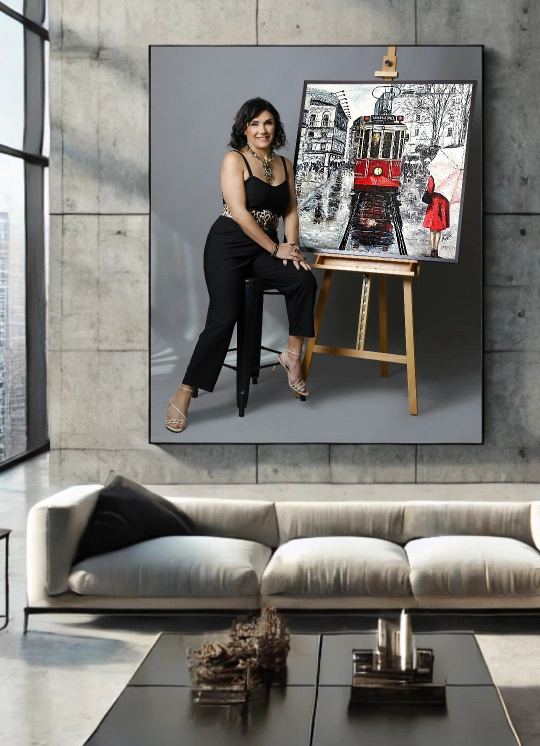 Woman sitting on a stool next to a painting of a tram on an easel in a modern living room.